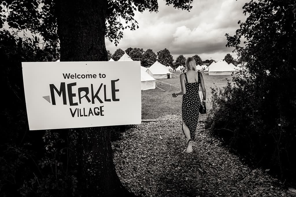 En kvinna som går mot tält och en skylt med texten Welcome to Merkle Village